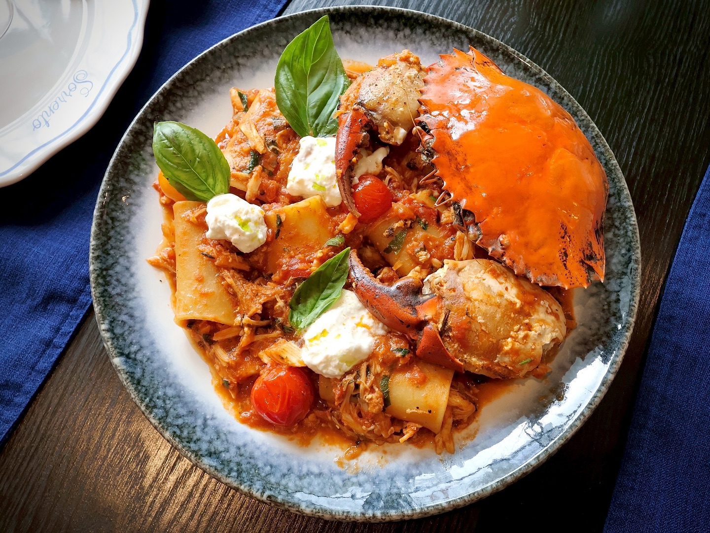 Large paccheri pasta in a rich tomato and crab sauce, topped with a whole cooked crab, dollops of creamy burrata cheese, and fresh basil leaves.